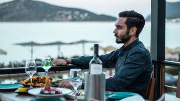 Una persona cenando en una mesa con vista al agua y montañas al fondo.
