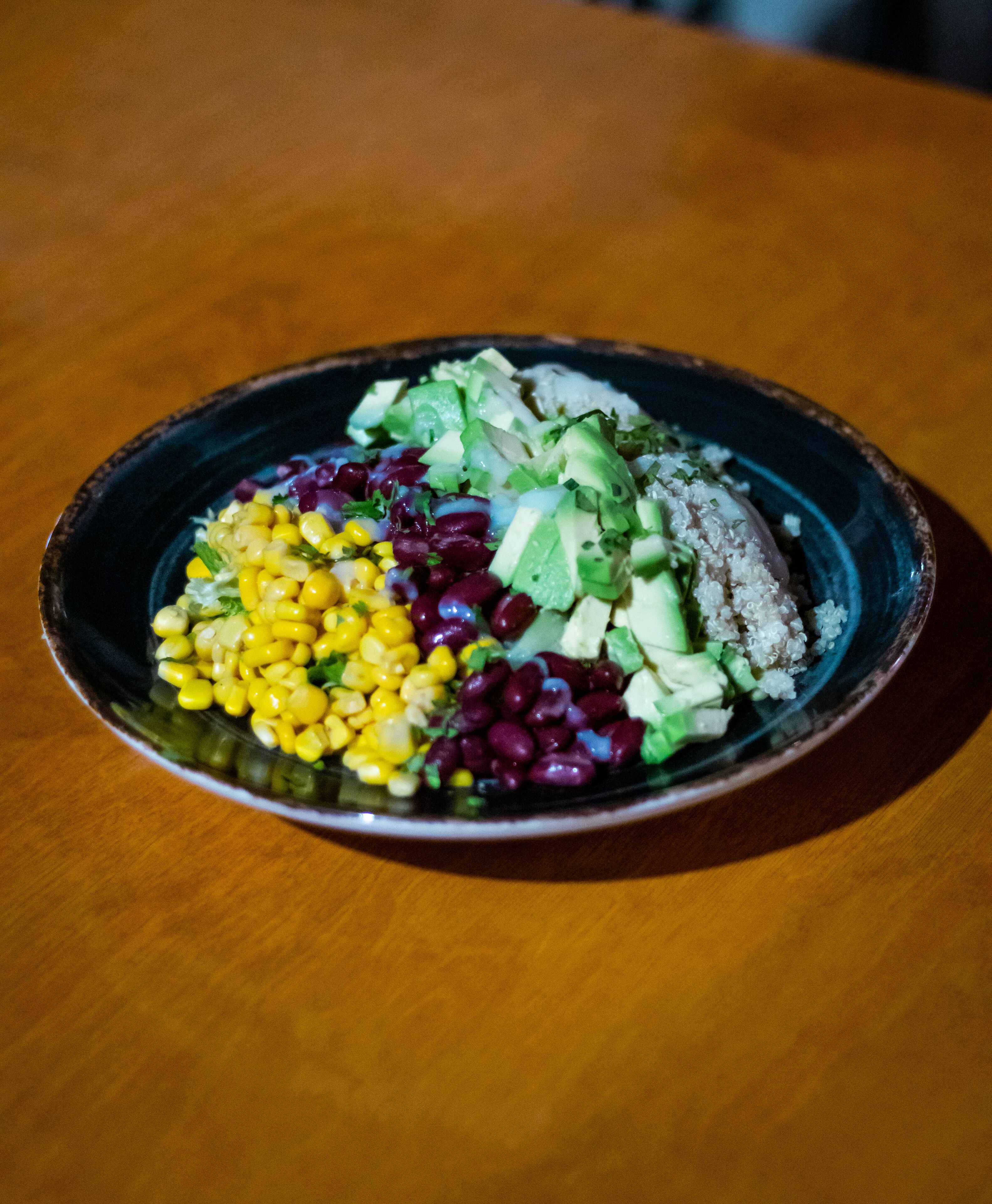 Een bord eten met mais, bonen, avocado en andere ingrediënten op een houten tafel.