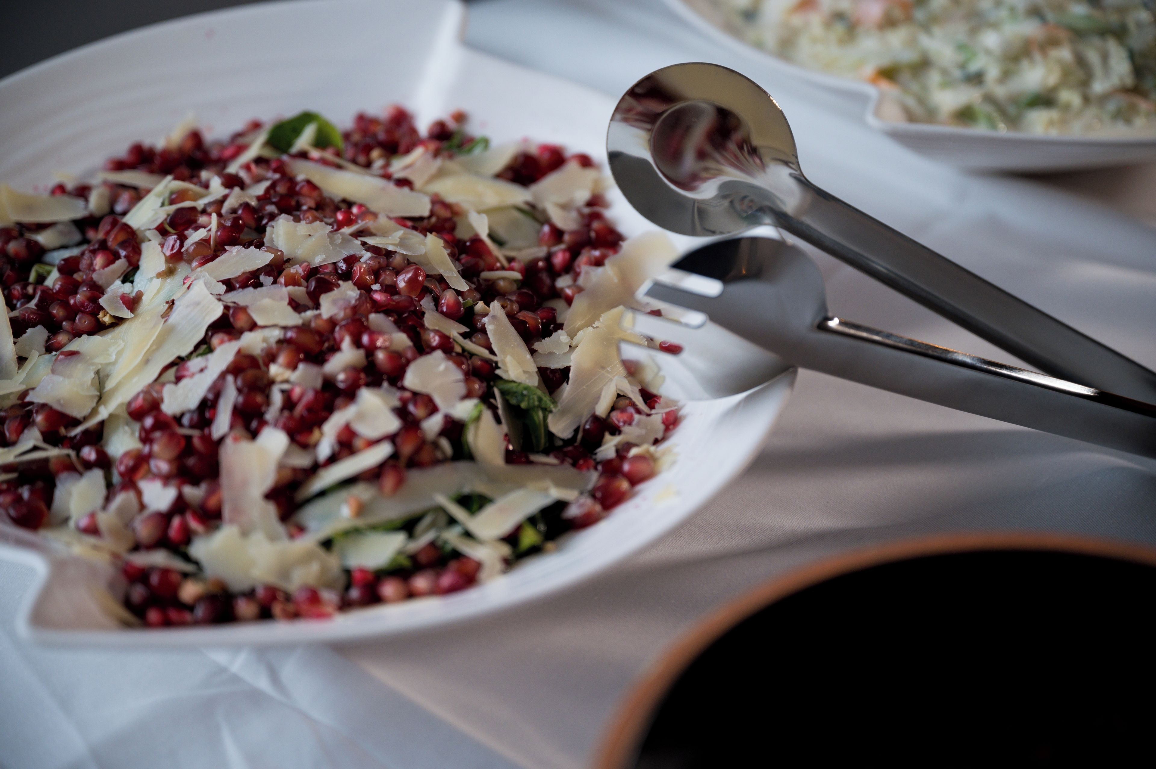 Ein weißer Teller mit Salat, einer Gabel und einem Löffel auf einem Tisch.