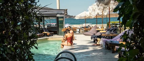 A poolside area with lounge chairs and umbrellas, a clear view of the sea, and a tall structure in the background.
