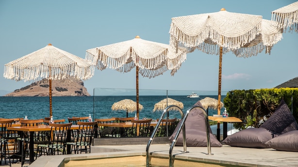 Ein Poolbereich mit Liegestühlen, Sonnenschirmen und Tischen mit Blick auf das Meer.