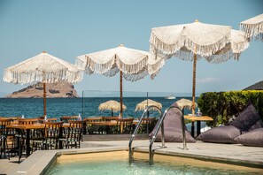 Un espace aménagé au bord de la piscine, avec des chaises longues, des parasols et des tables offrant une vue sur la mer.