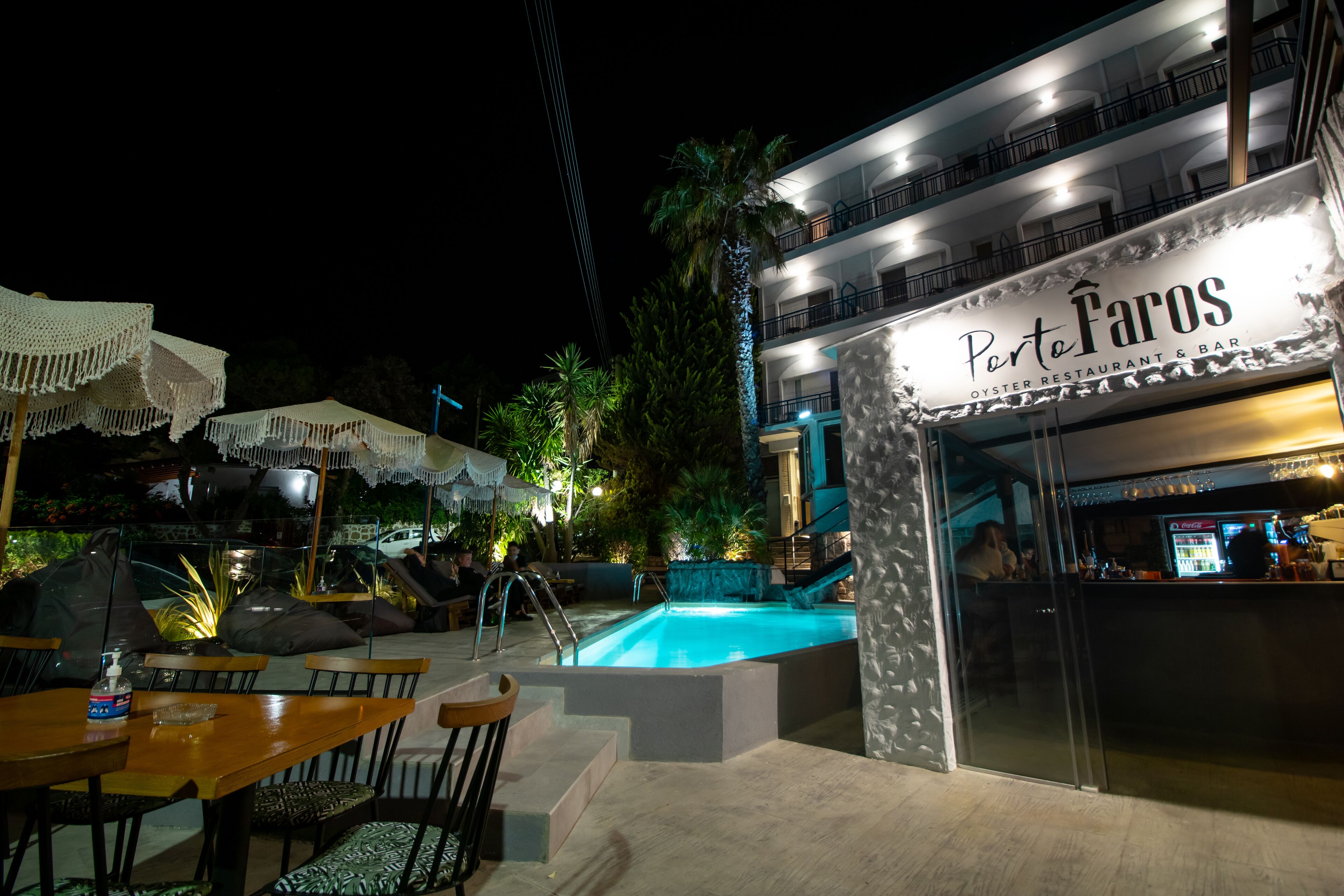 An outdoor pool area with a bar and restaurant named "Porto Faros" adjacent to it.