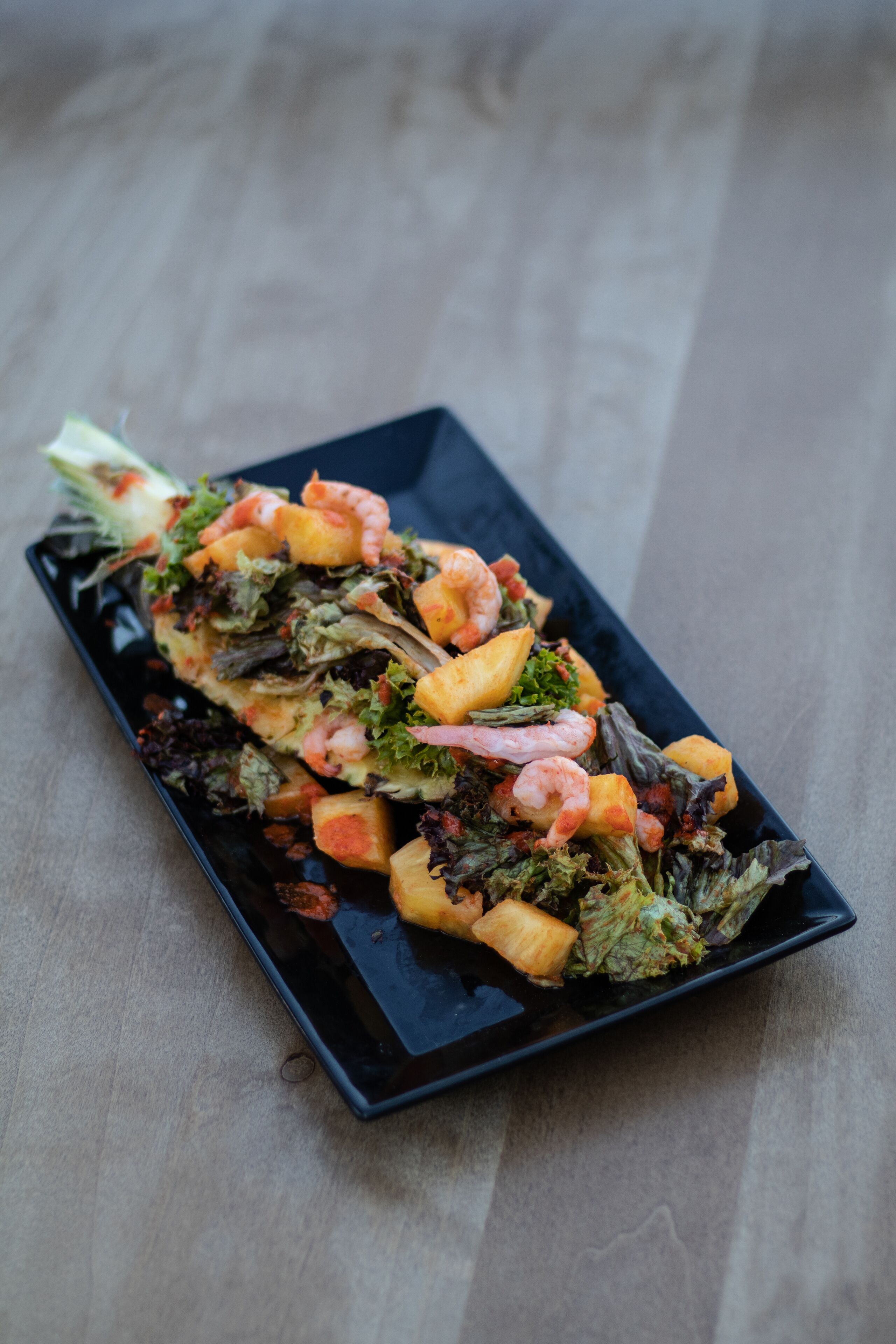 A rectangular black plate with a seafood salad on a wooden table.