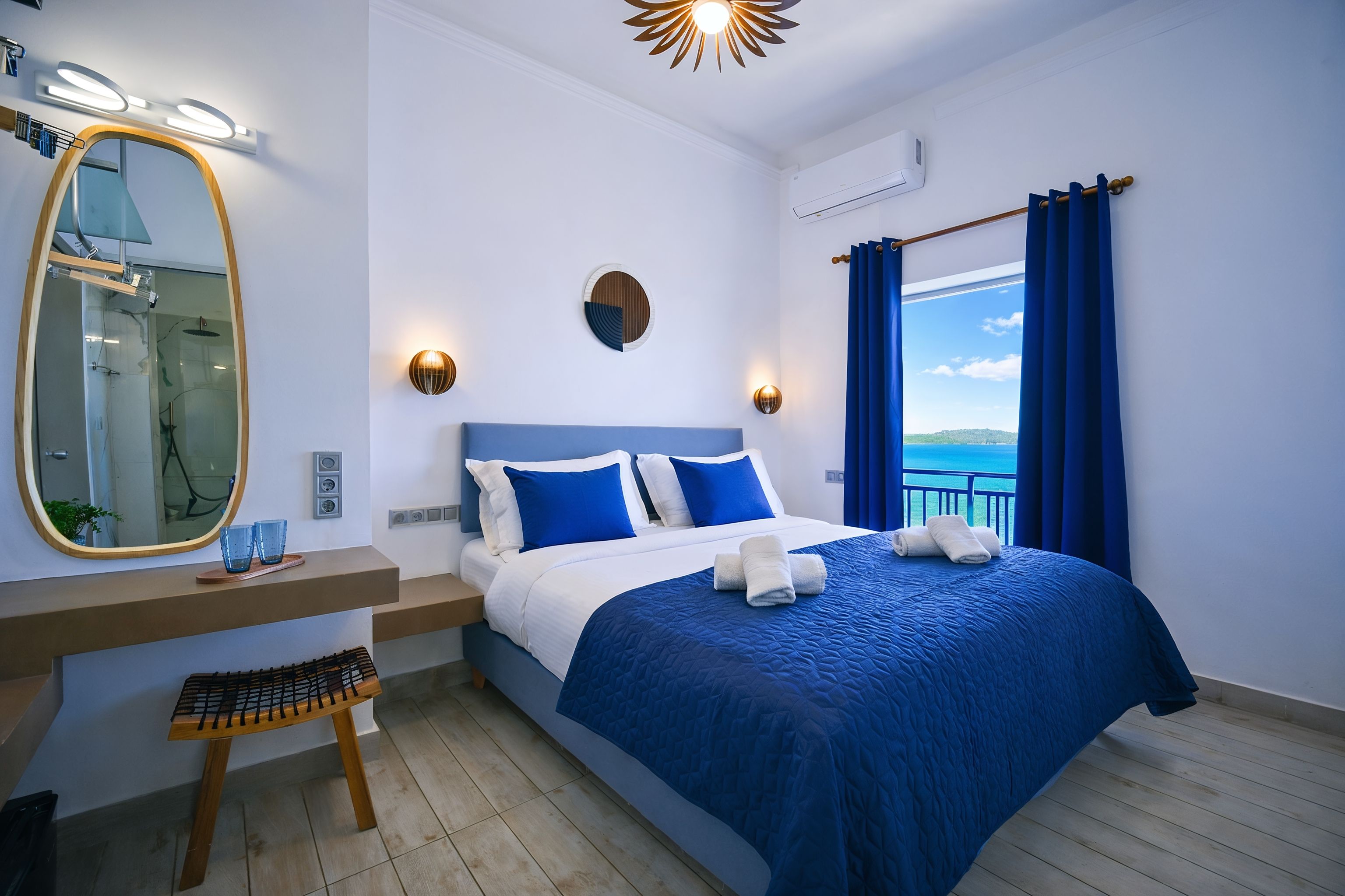 Habitación de hotel moderna con una cama grande, un espejo de baño y vistas al mar.