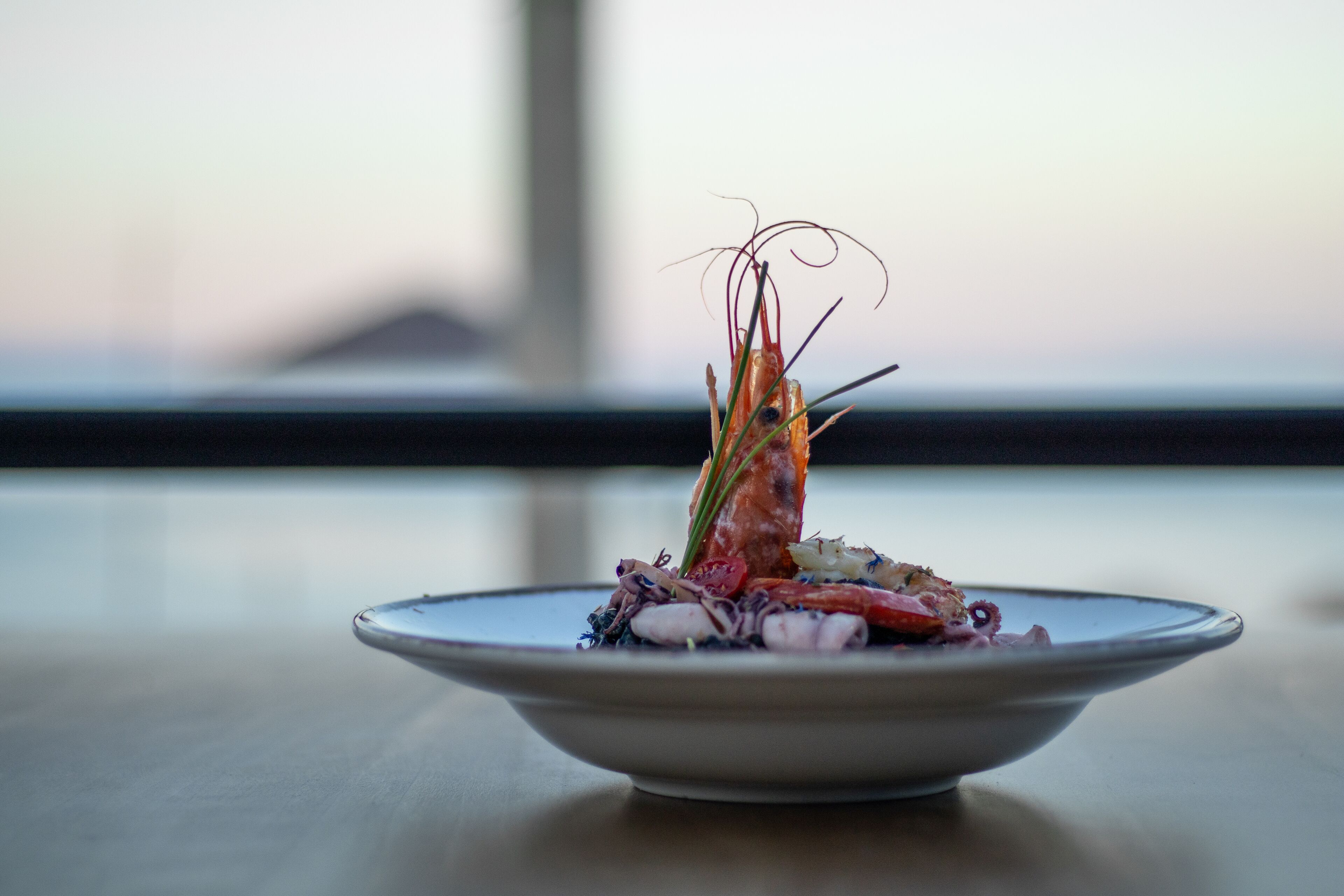 A plate of food with a shrimp centerpiece, placed on a table with a blurred background.