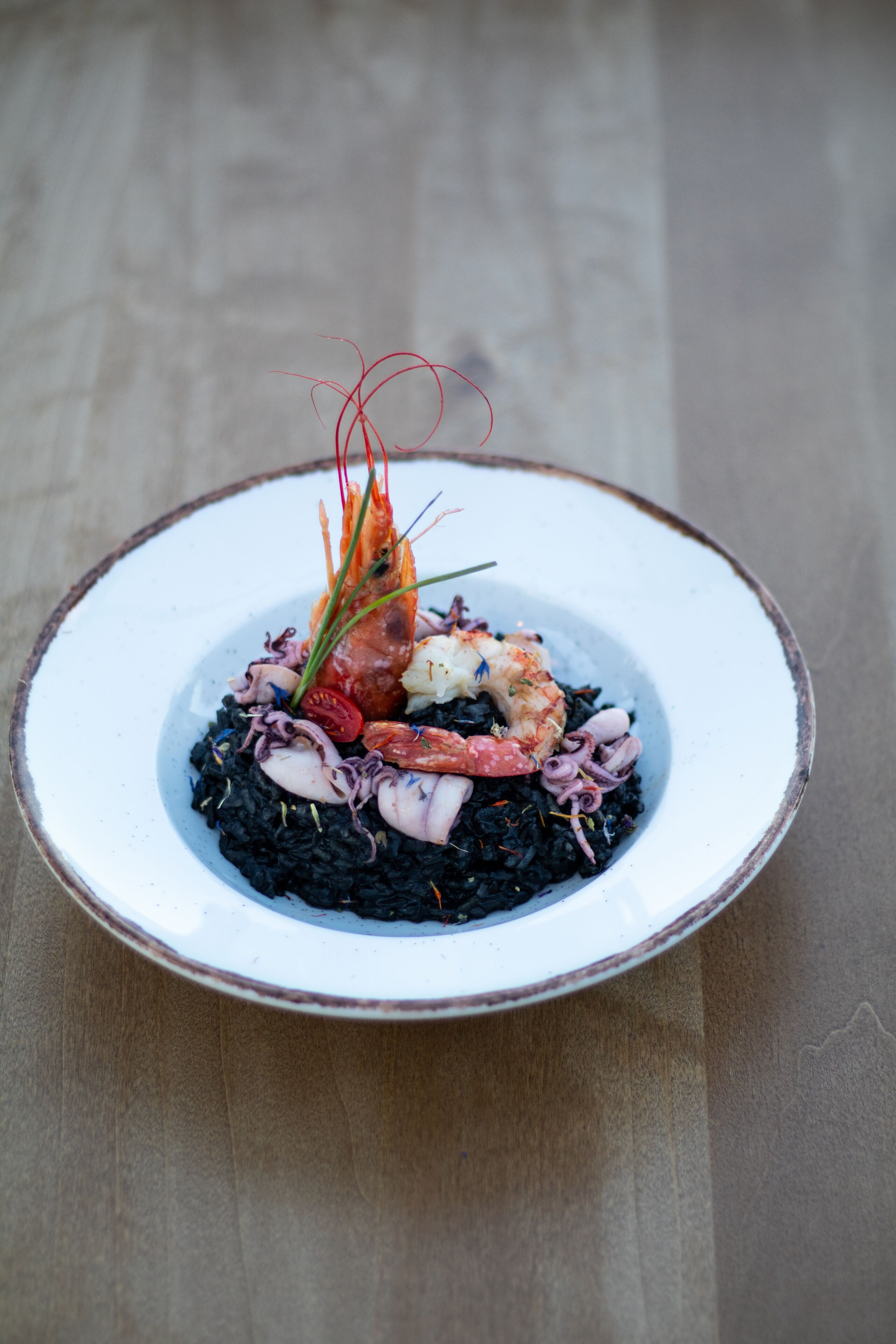 Eine Portion schwarzes Risotto mit Garnelen und Tintenfisch, garniert mit Kräutern und einem dekorativen Element.
