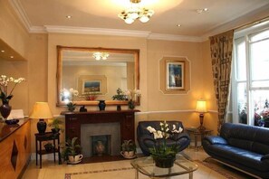 A well-lit living room with a fireplace, a large mirror, a sofa, and a coffee table. - Avon Hotel (London)