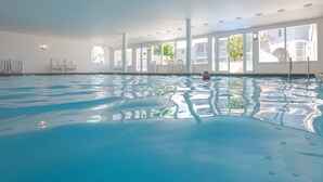 Une piscine intérieure à l’eau claire, avec des murs blancs et de grandes fenêtres.