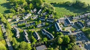 Vue aérienne d’un quartier résidentiel avec de nombreuses maisons à deux étages, un parking et des espaces verts environnants.