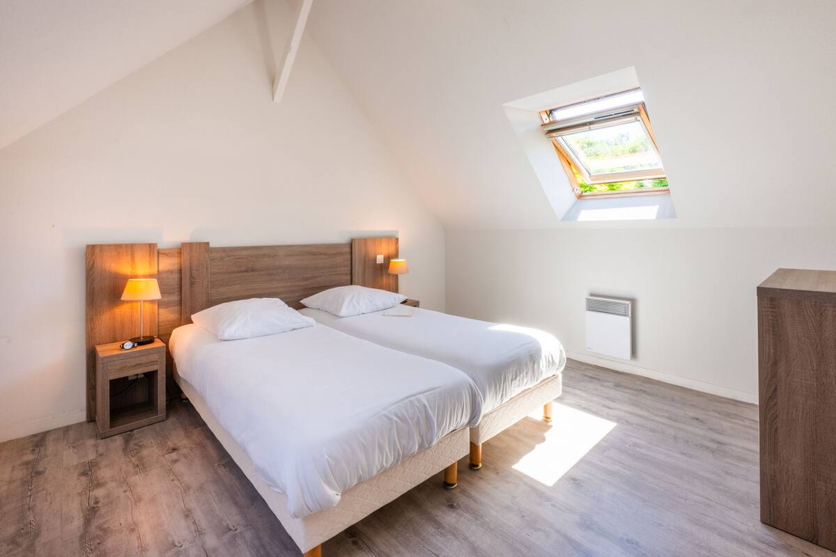 Un dormitorio con dos camas, un tragaluz, suelo de madera y lámparas de noche.