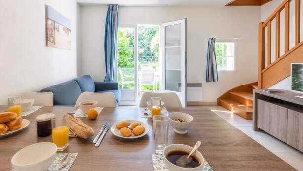 Un salon moderne avec un coin repas, comprenant un canapé, une table basse et un buffet pour le petit-déjeuner avec des croissants, du jus et du café.