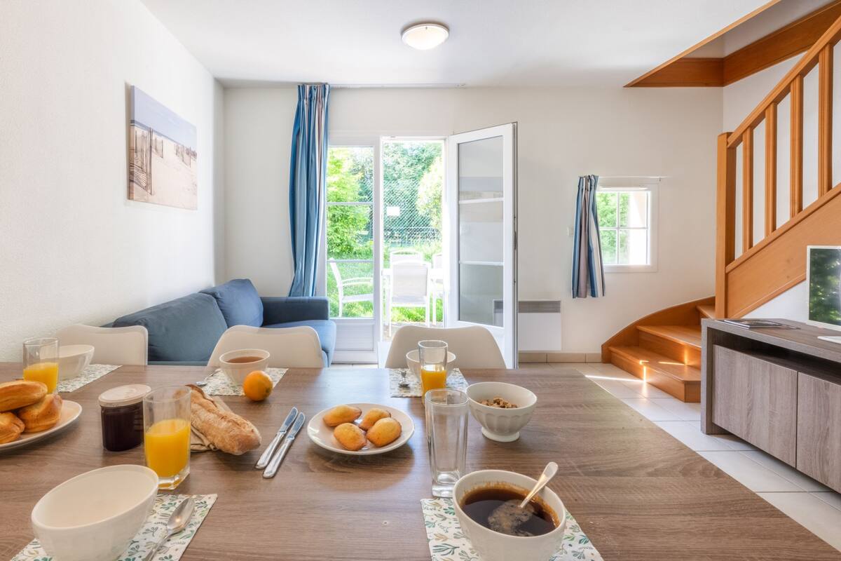 Un salón moderno con comedor, que incluye un sofá, una mesa de centro y un espacio para desayunar con cruasanes, jugo y café.