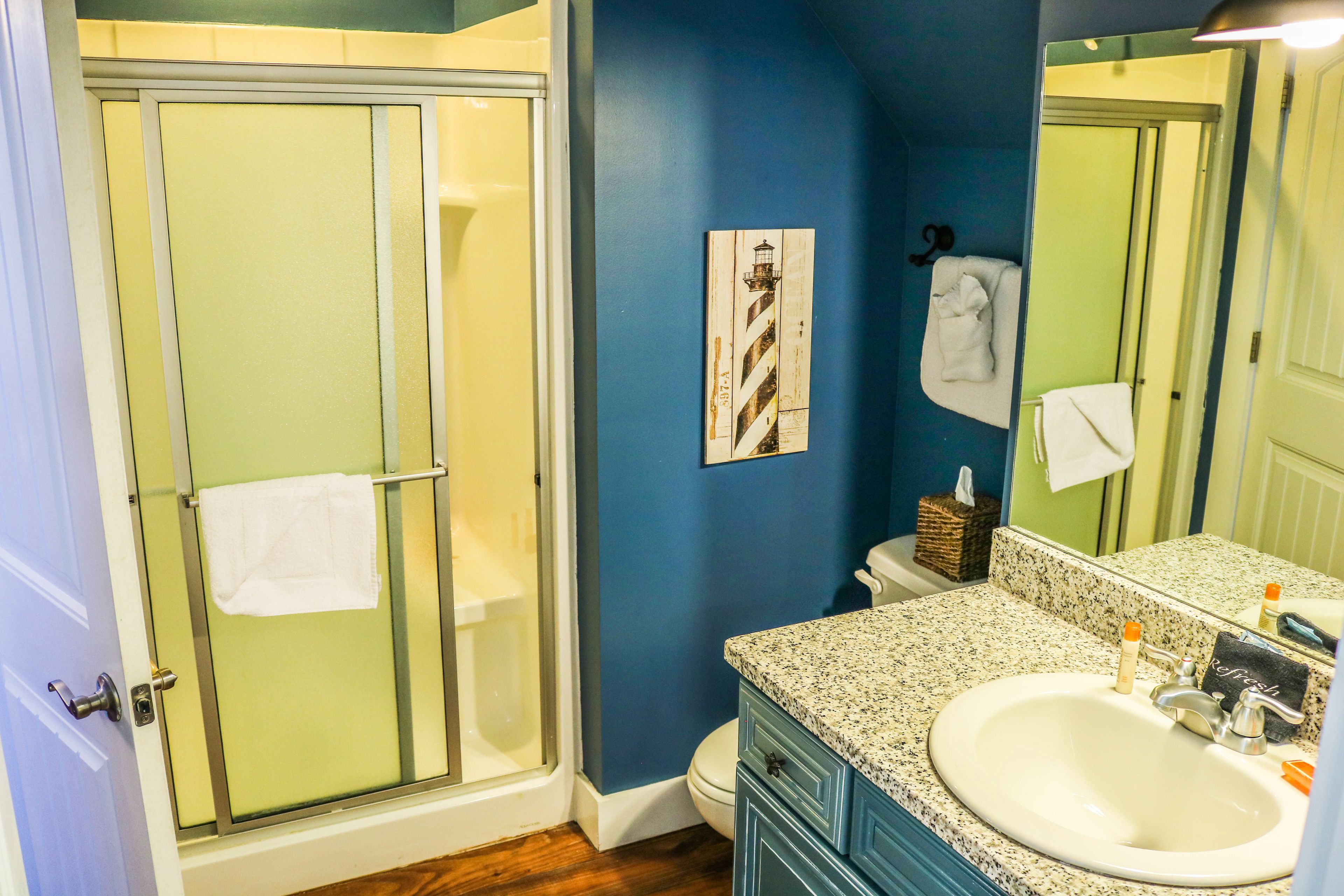 Un baño con mampara de vidrio, lavabo con encimera de granito y espejo que refleja la habitación.