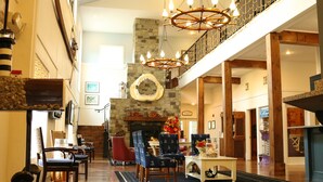 A spacious lobby with a high ceiling, a stone fireplace, and a chandelier. There are multiple seating areas with chairs and tables.