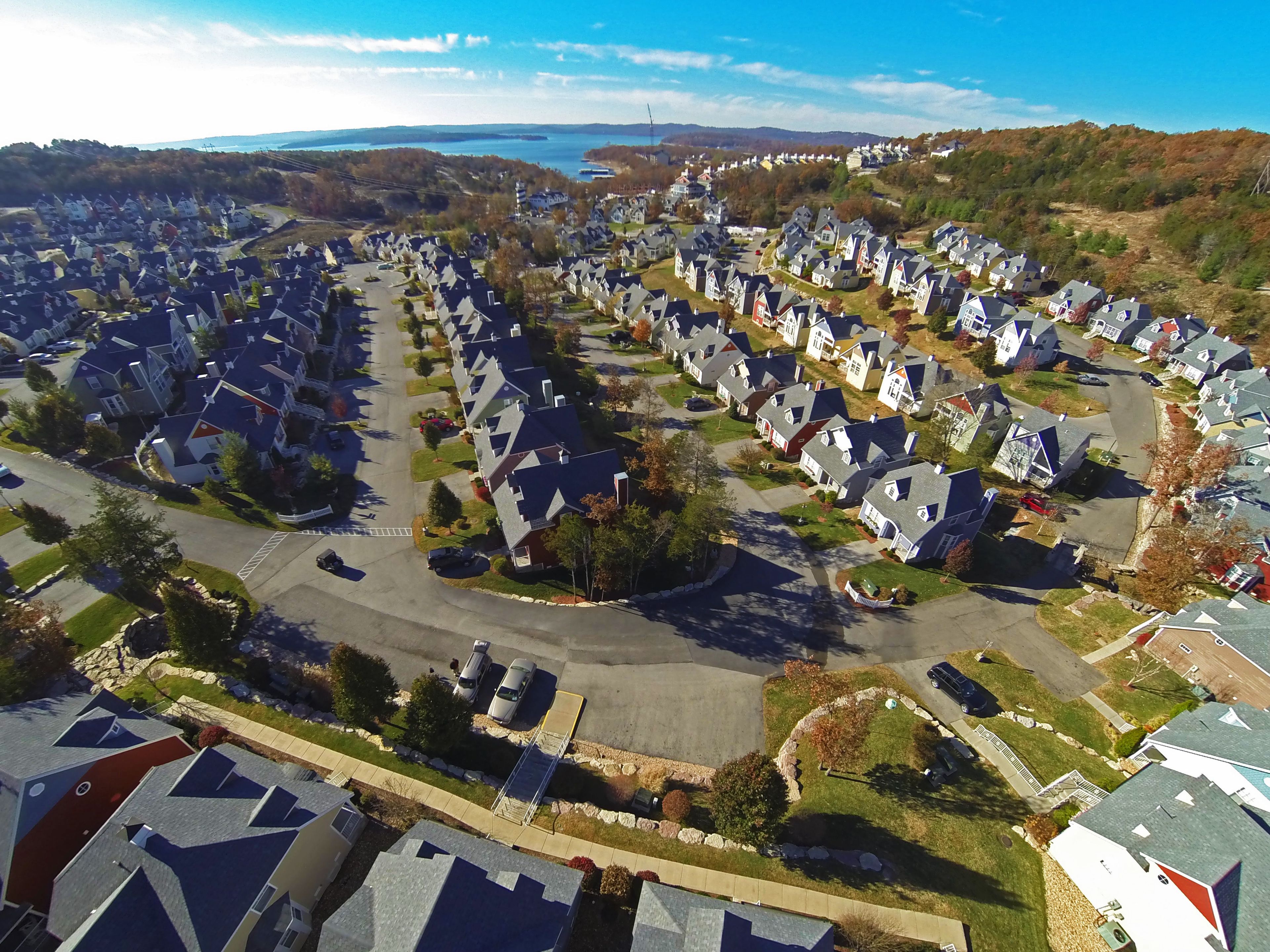 Un quartier résidentiel où les maisons sont alignées le long d’une route principale, entouré de verdure et avec une étendue d’eau en arrière-plan.