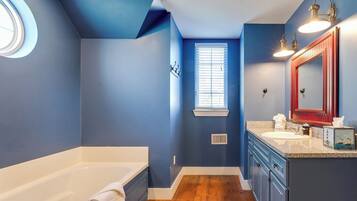 A bathroom with a bathtub, a window, and a vanity with a mirror.