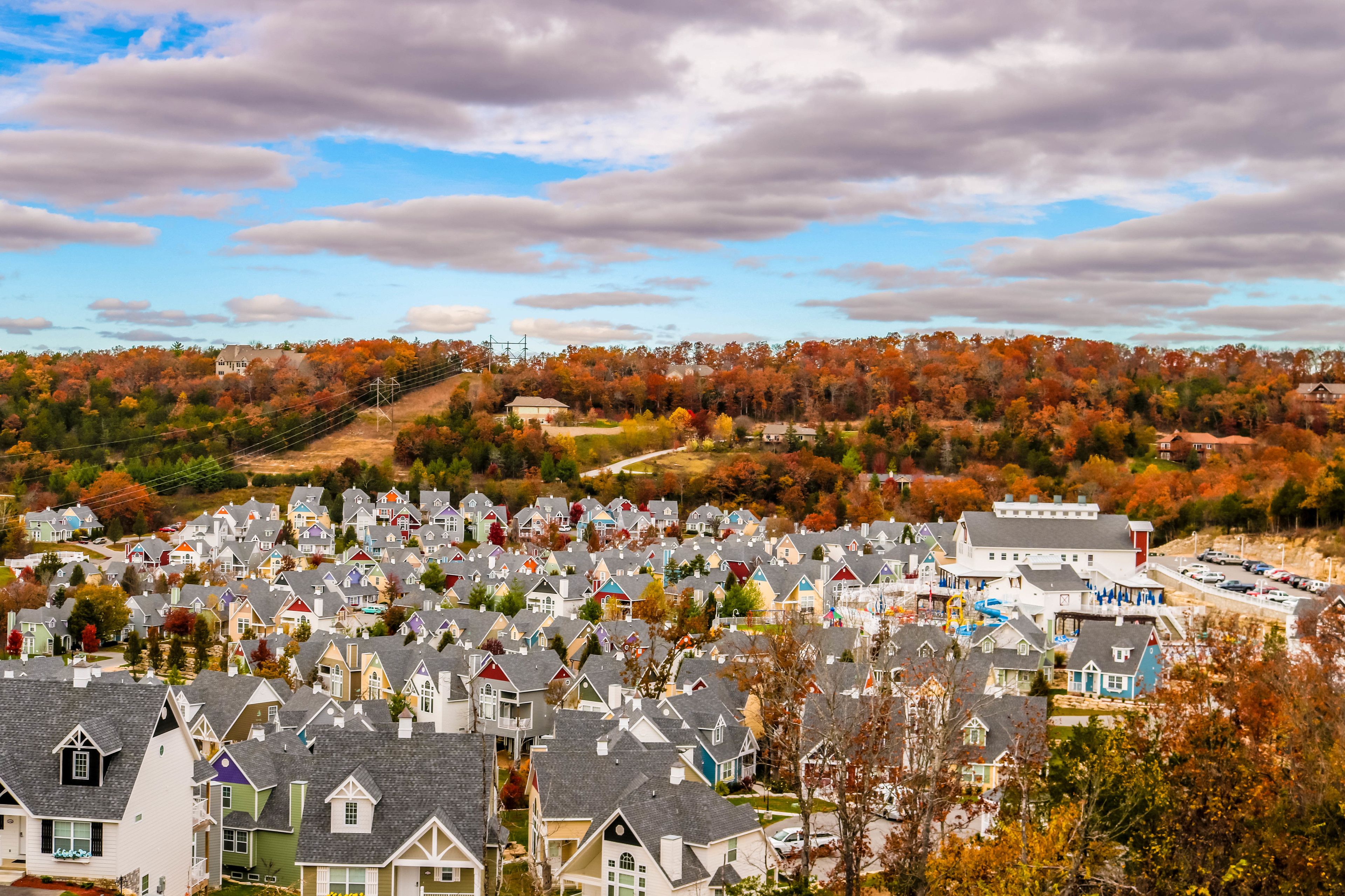 A residential area with houses and a large building, surrounded by autumn-colored trees.