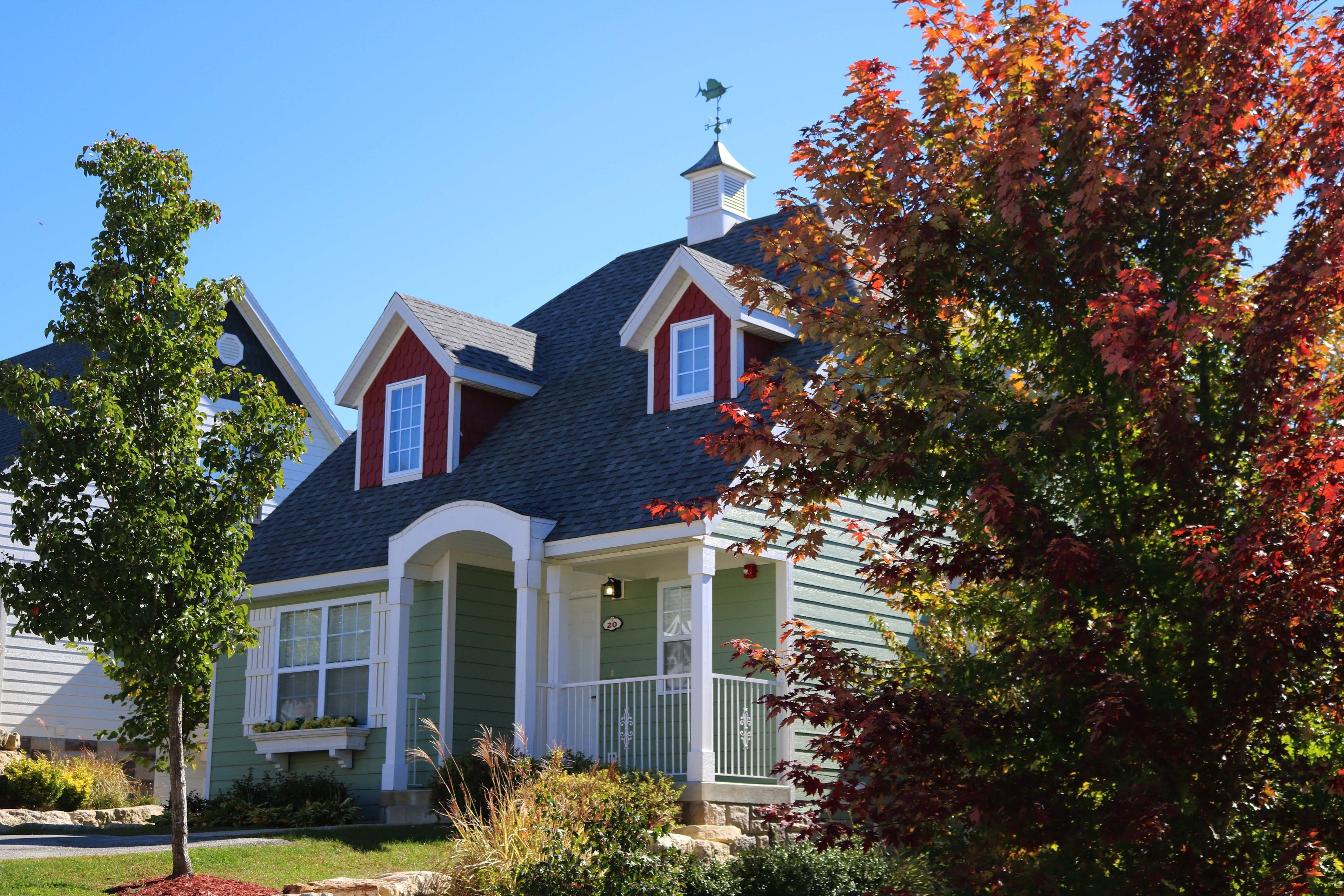 A two-story house with a green exterior, a dark roof, and a small porch with white railings.
