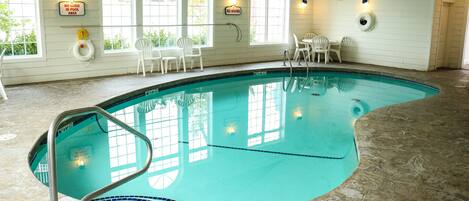 An indoor swimming pool with clear poolside chairs, a no diving sign, and a lifebuoy.