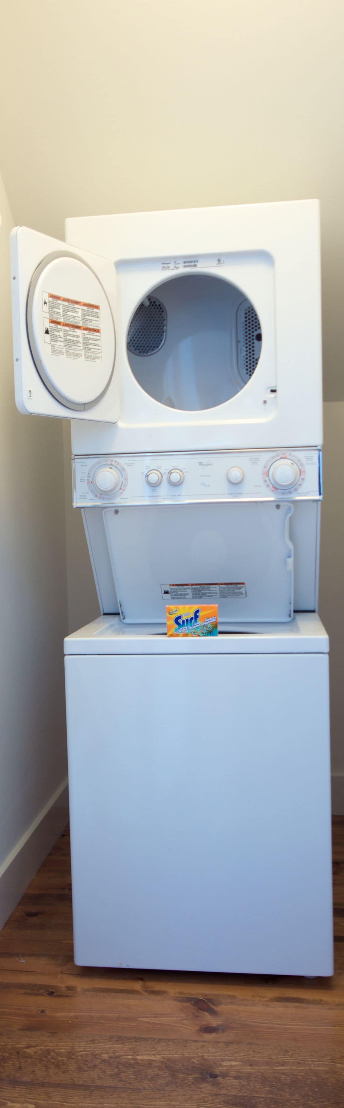 Une machine à laver blanche à chargement frontal, dotée d’un panneau de commande et d’un compartiment à lessive sur lequel est inscrit le mot « Surf ».