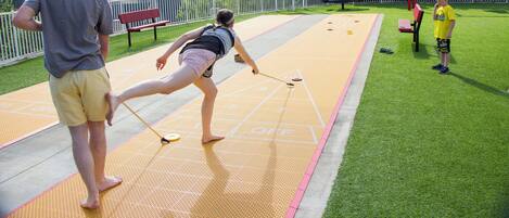 Un terrain de jeu de shuffleboard avec des joueurs et un spectateur.