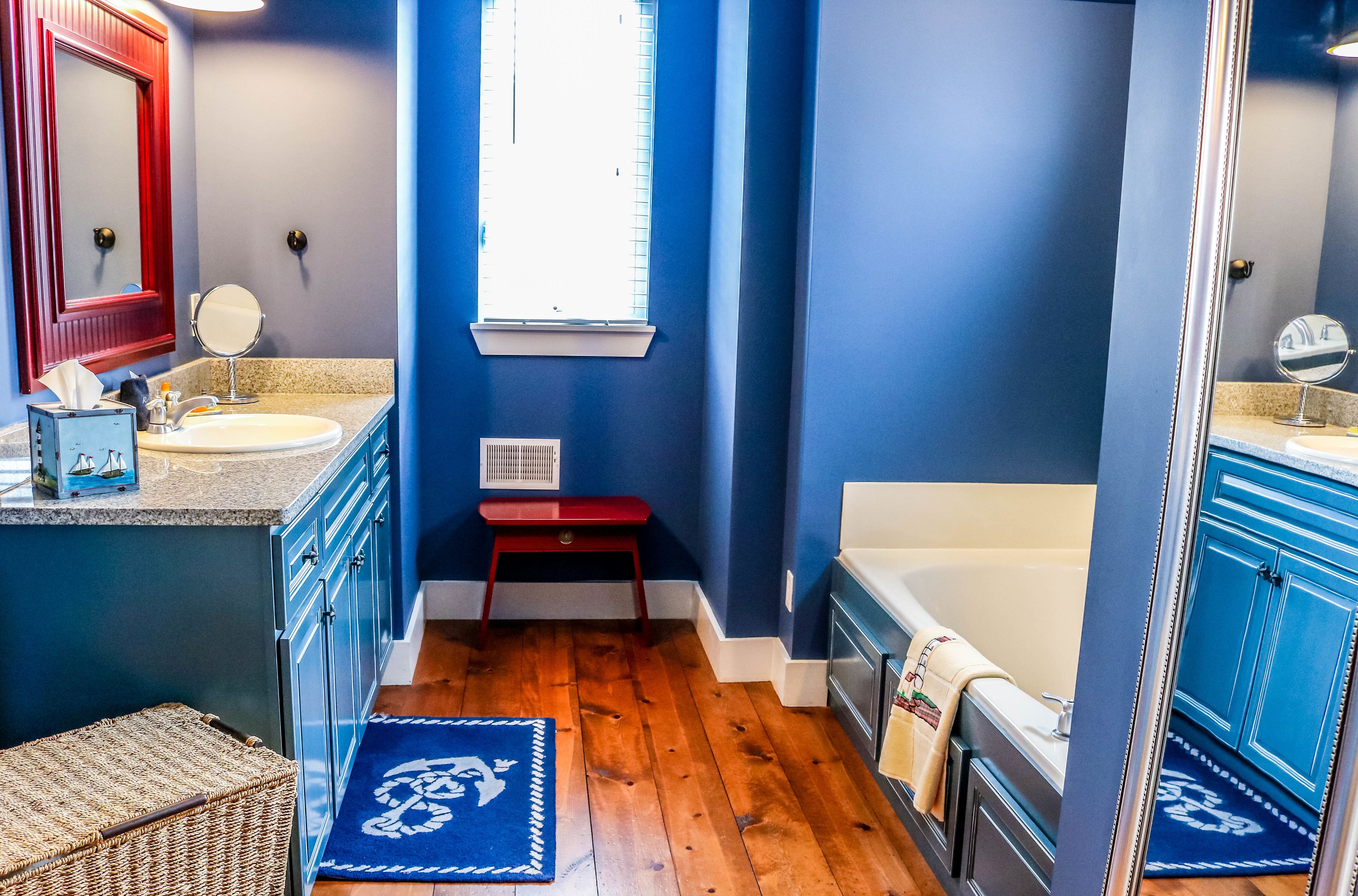 A bathroom with a bathtub, two sinks, a mirror, a window, and a wooden floor.