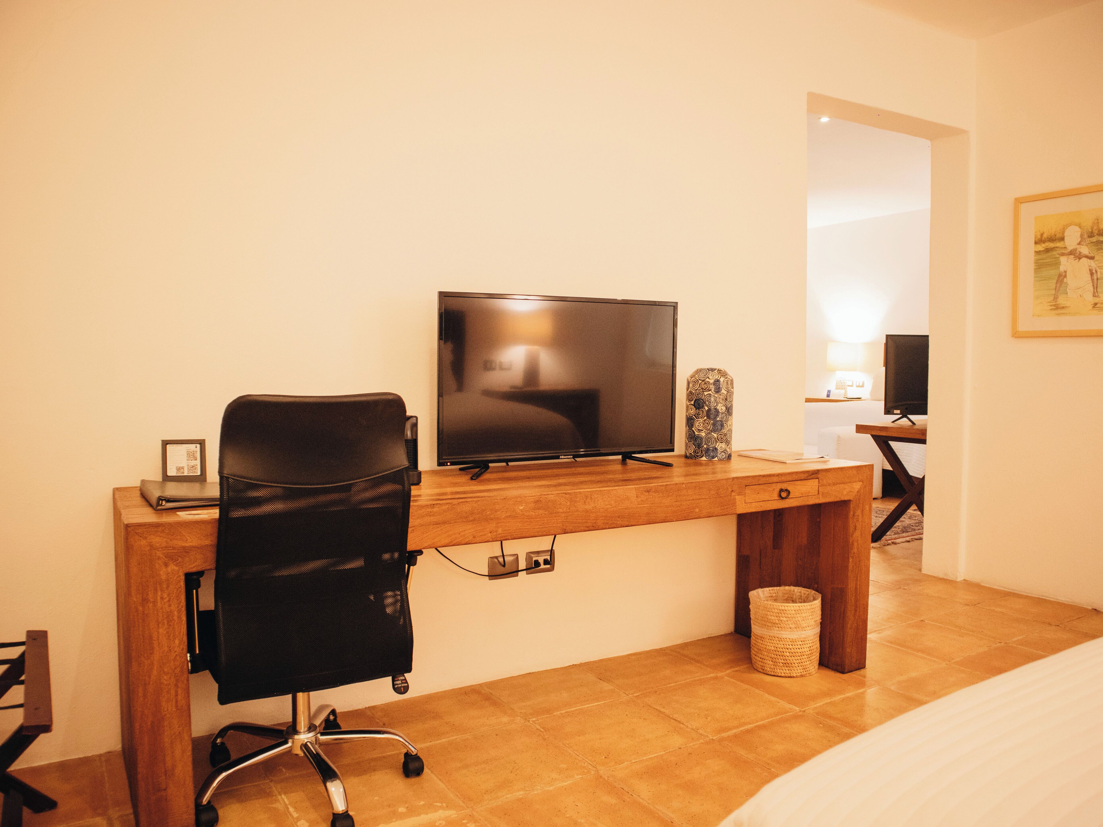 A hotel room with a wooden desk, a black office chair, a television, and a framed picture on the wall.