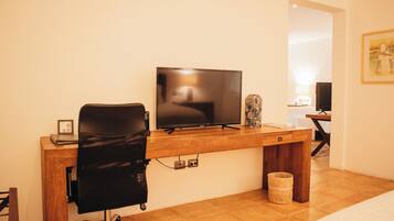 Una habitación de hotel con un escritorio de madera, una silla de oficina negra, un televisor y un cuadro en la pared.