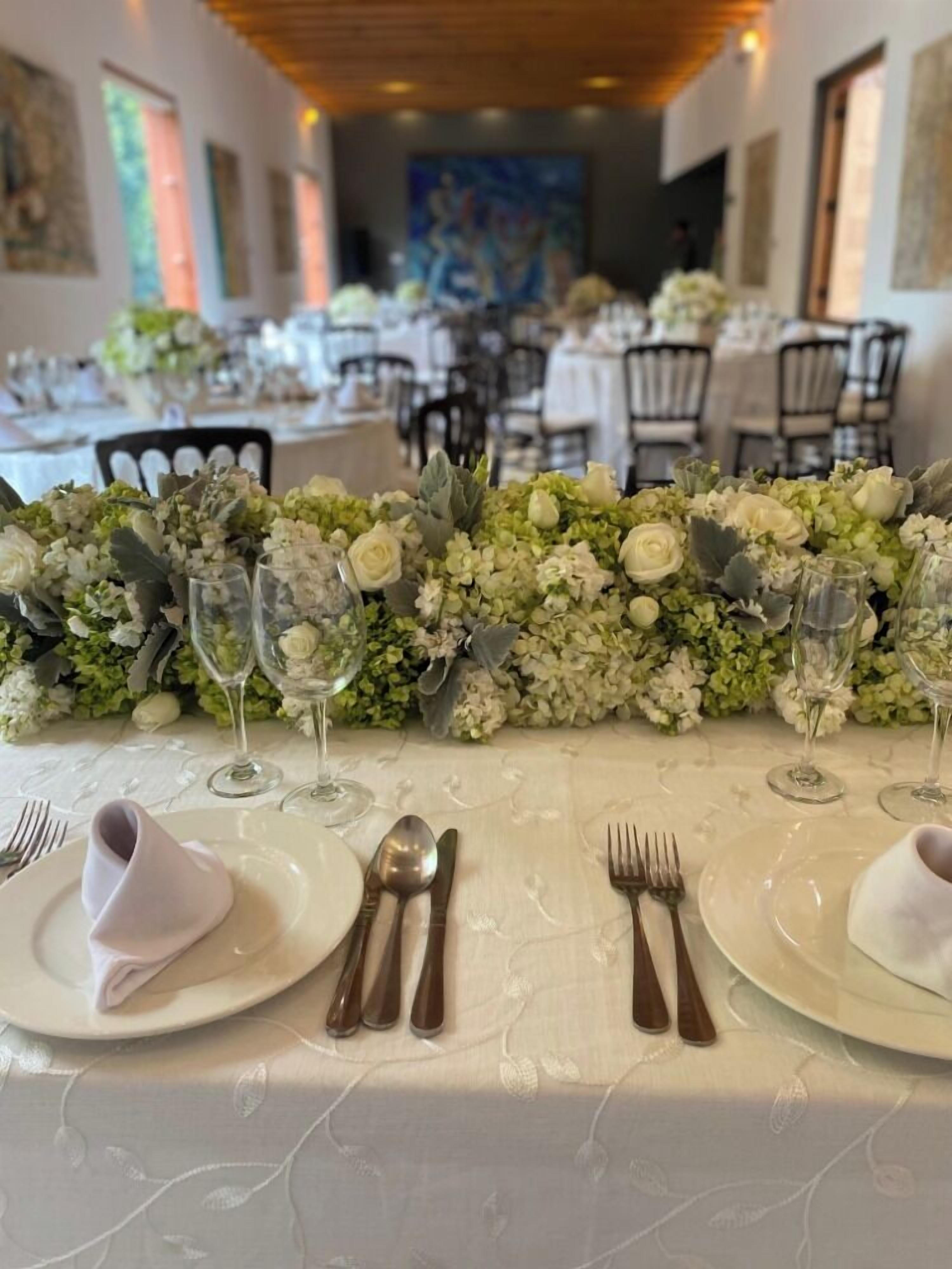 Un comedor con mesas dispuestas para un evento formal, con manteles blancos, centros de mesa florales y cubertería.