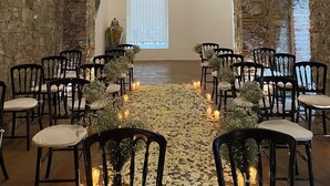 An indoor venue with an arched stone wall, black chairs arranged in rows, a central aisle with flower petals, and hanging floral decorations. - Hotel Boutique Casareyna (Puebla)