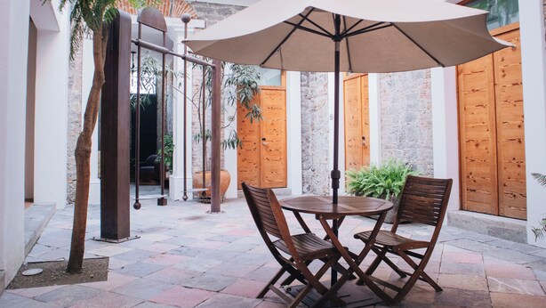 An outdoor patio with a round table and chairs, a large umbrella, and wooden doors. - Hotel Boutique Casareyna (Puebla)