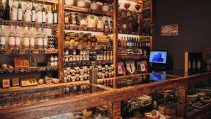 Un espace bar avec des étagères remplies de bouteilles et de pots de toutes sortes, un écran de télévision et une vitrine où sont exposées des pâtisseries.