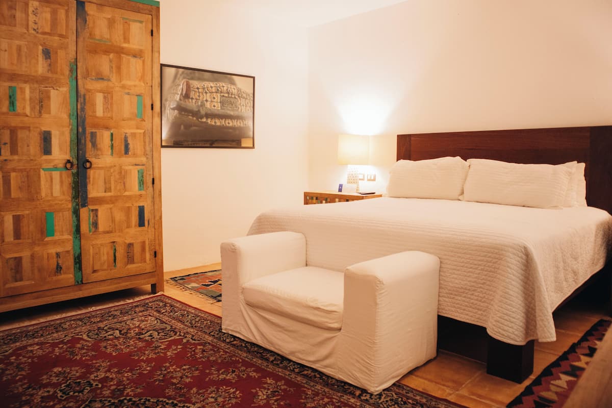 Un dormitorio con cama, una silla, una mesita de noche, una lámpara y un armario.