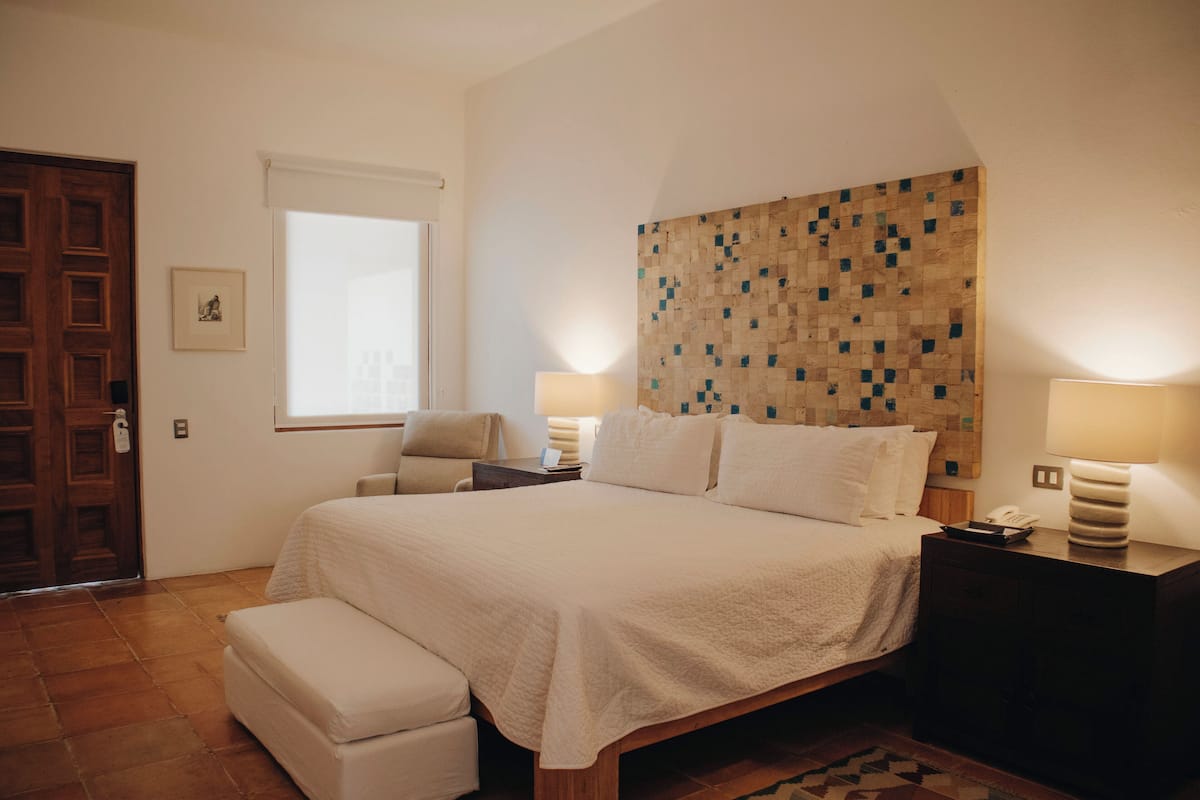 Un dormitorio con cama, mesitas de noche, una silla, una ventana y cabecera de madera con diseño de mosaico.