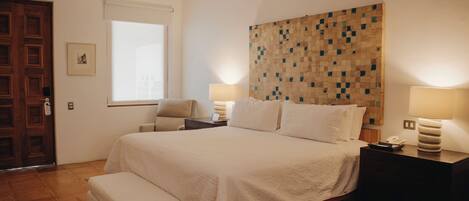 Un dormitorio con cama, mesitas de noche, una silla, una ventana y cabecera de madera con diseño de mosaico.