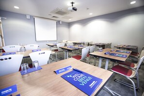 Host meetings and presentations in a professional setting with tables, chairs, projector screen, and ceiling speakers.