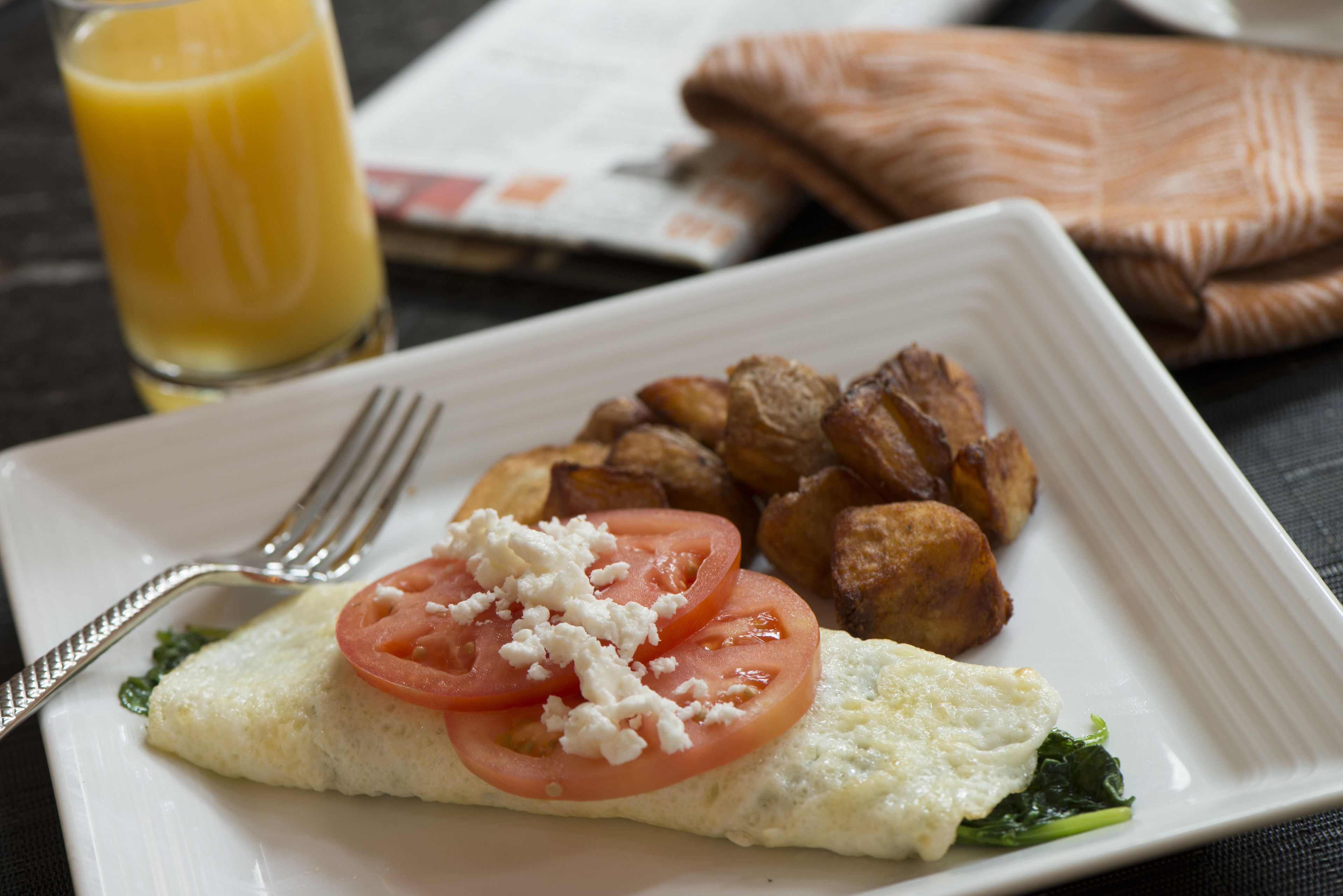 A breakfast plate with eggs, tomatoes, feta cheese, and roasted potatoes.