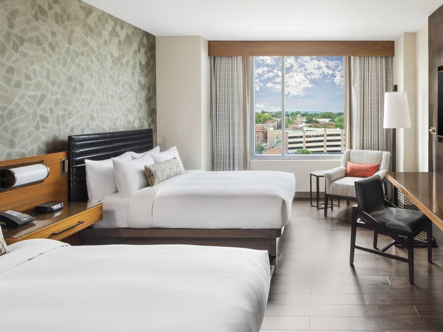 A hotel room with two beds, a desk, a chair, and a TV.