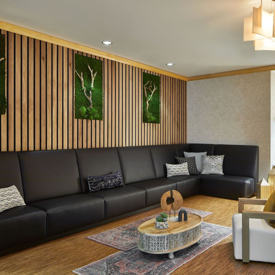 A modern living room with a black leather sofa, a round coffee table, and a wooden accent wall with vertical slats.