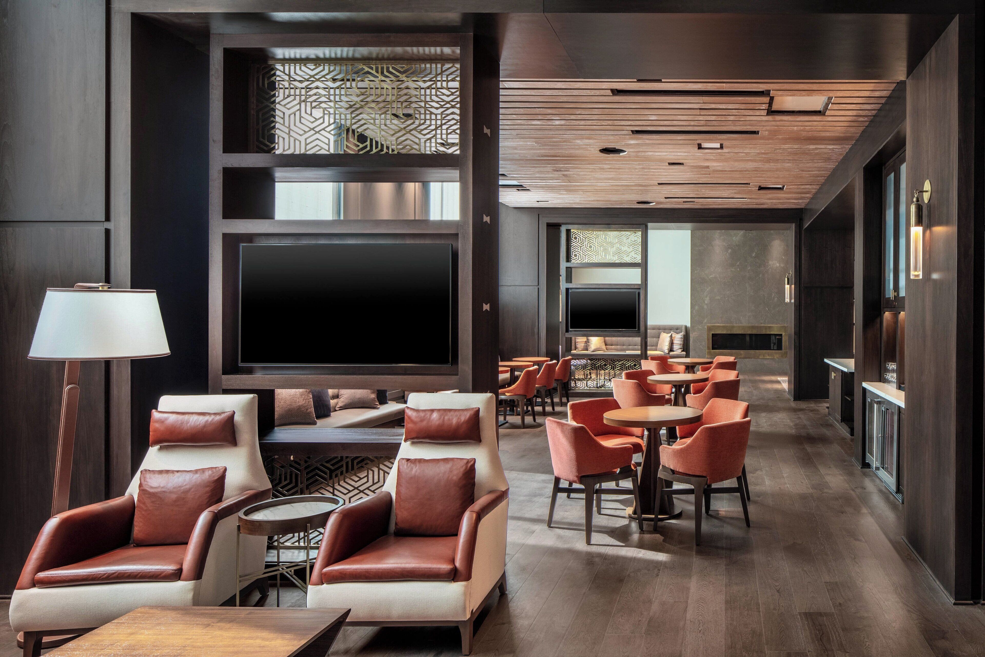 A modern lounge area with leather armchairs, a flat-screen TV, and a bar area with orange chairs and tables.