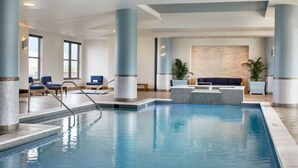 Una piscina interior con agua azul cristalina, rodeada de sillas de descanso y una zona de estar con un muro de piedra de fondo.