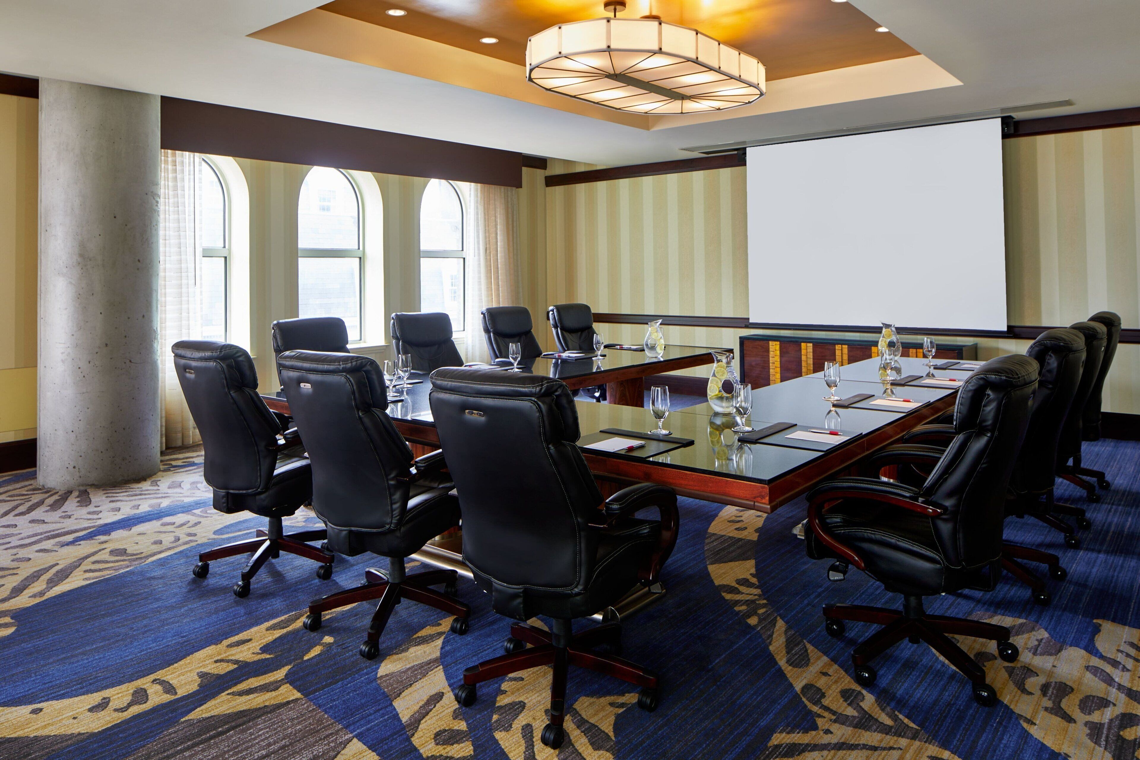 Un salón de conferencias con una larga mesa, varias sillas y una pantalla de proyector.