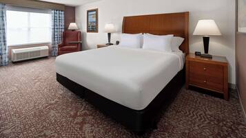 Una habitación de hotel con una cama grande, dos mesitas de noche con lámparas, una silla, un ventanal con cortinas y un cuadro colgado en la pared.