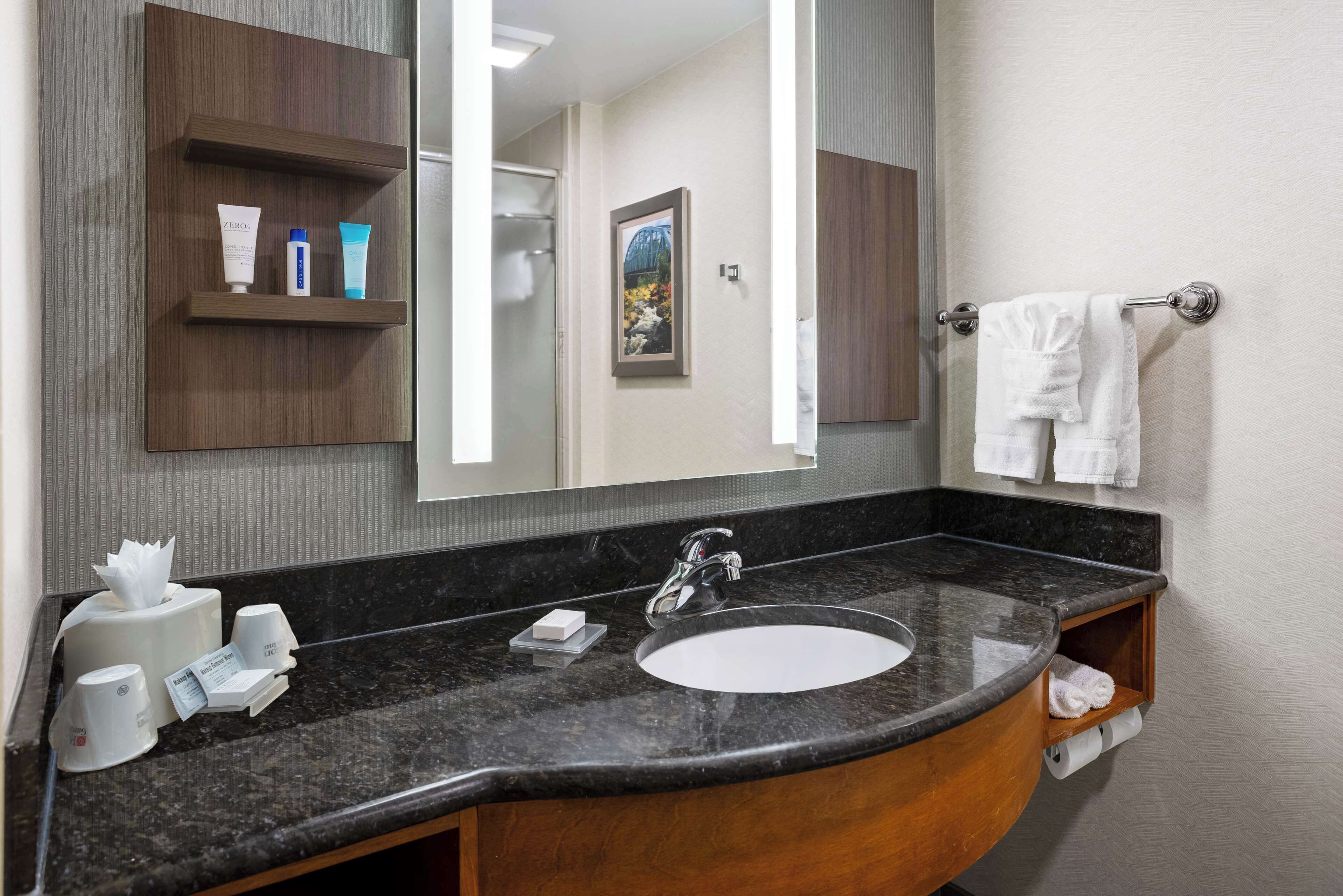 Un baño con un espejo grande, un lavamanos y un perchero para toallas.