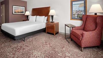 Habitación de hotel con cama, dos mesitas de noche con lámparas, un sillón rojo, una pequeña mesita auxiliar y dos cuadros en las paredes.