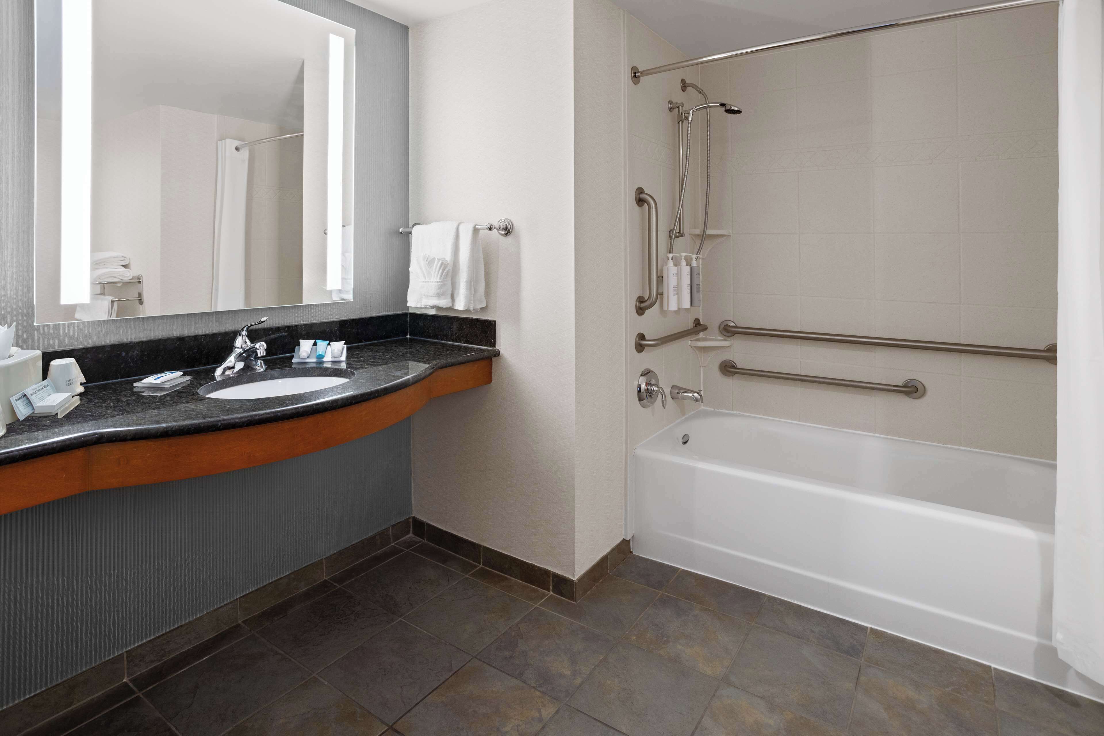 A modern bathroom with a sink, mirror, and a walk-in shower with grab bars.