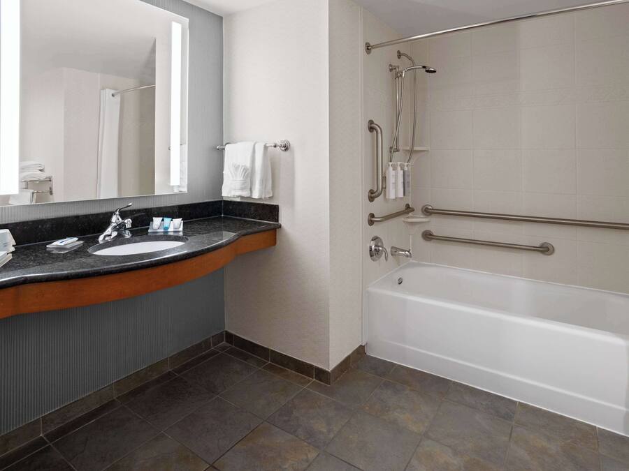 A modern bathroom with a sink, mirror, and a walk-in shower with grab bars.