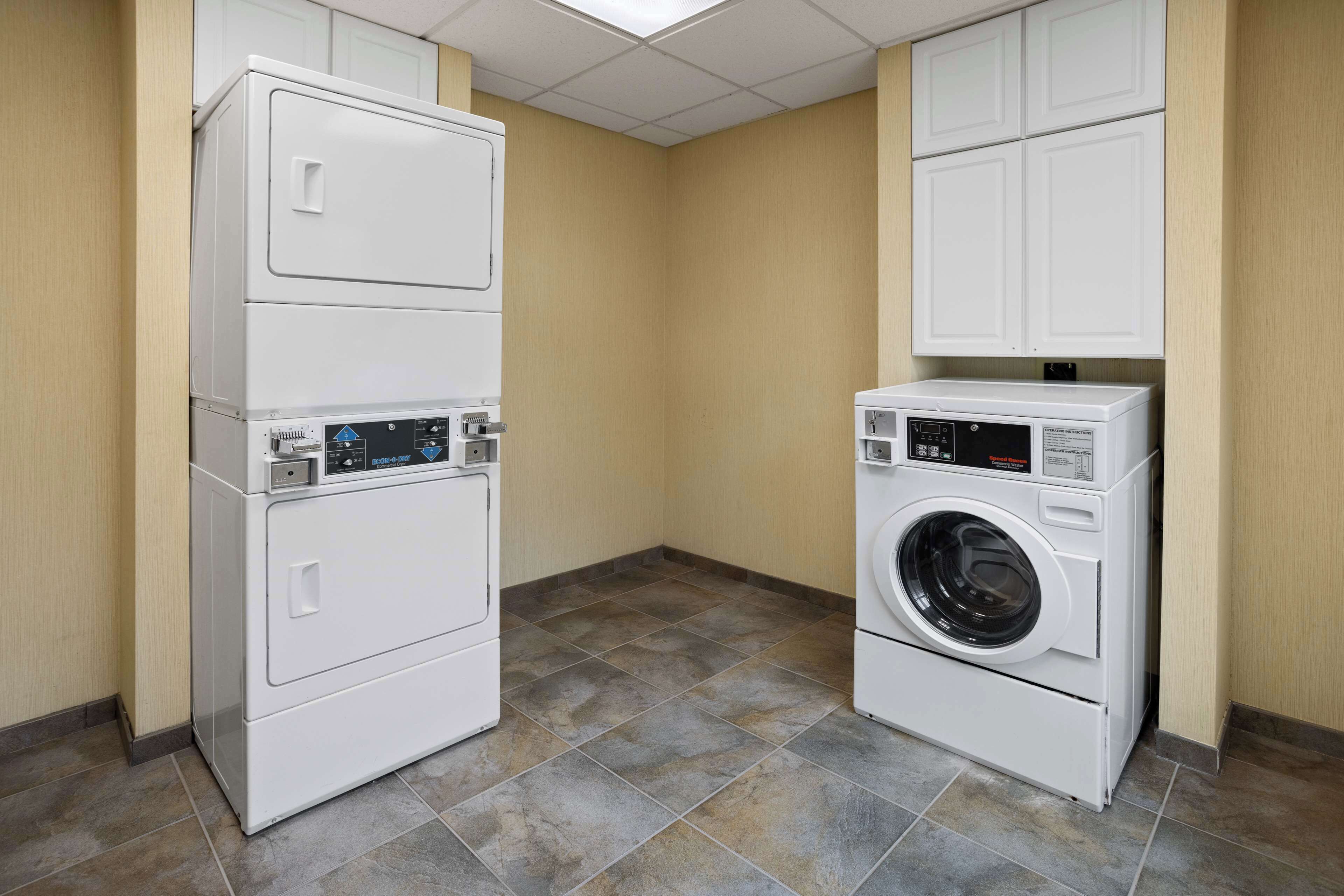 A laundry room with stacked washer and dryer units, beige walls, and tiled flooring.