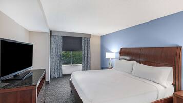 A hotel room with a bed, a TV, a nightstand, a lamp, and a window with curtains.